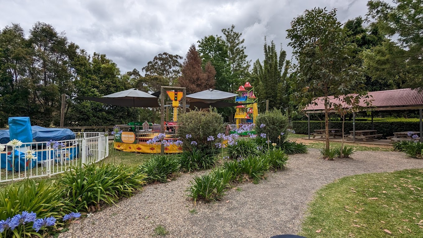 Garden path past small fairground rides and a picnic shelter at Amazement Farm & Fun Park