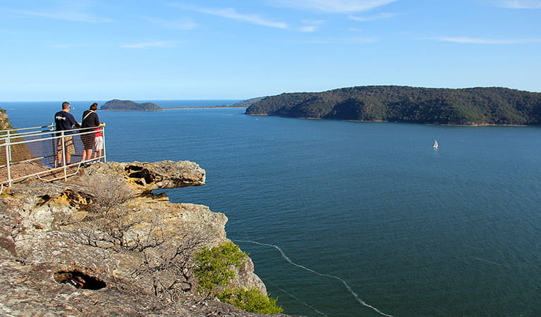 Visitors look out from a fenced sandstone lookout over Broken Bay in Brisbane Water National Park