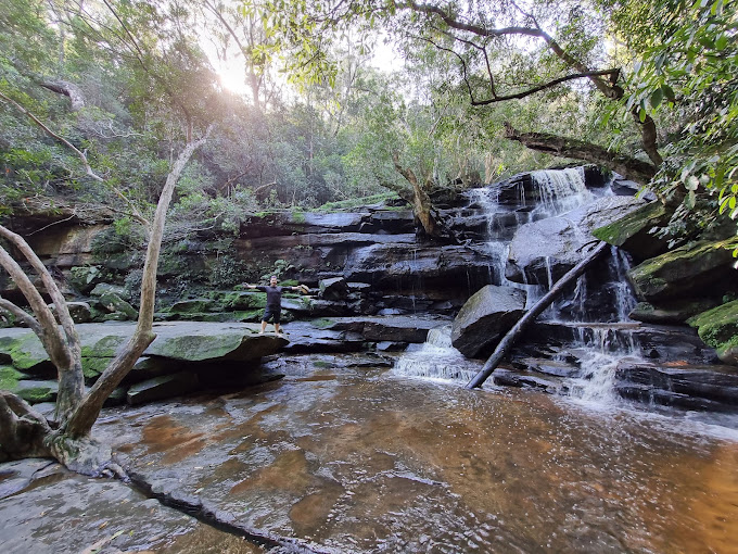 Water cascading over moss-covered rock ledges at Somersby Falls, with a walker standing nearby